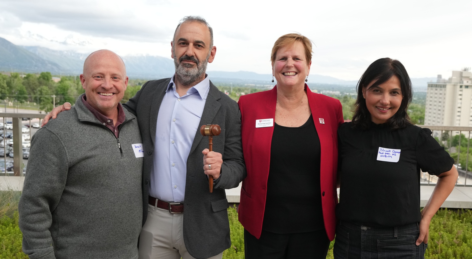 Drs. Brent Milne, Richard Preiss, Harriet Hopf, and Shanti Deemyad pose for a group picture outdoors, smiling at the camera and wearing name tags. Preiss holds a gavel.