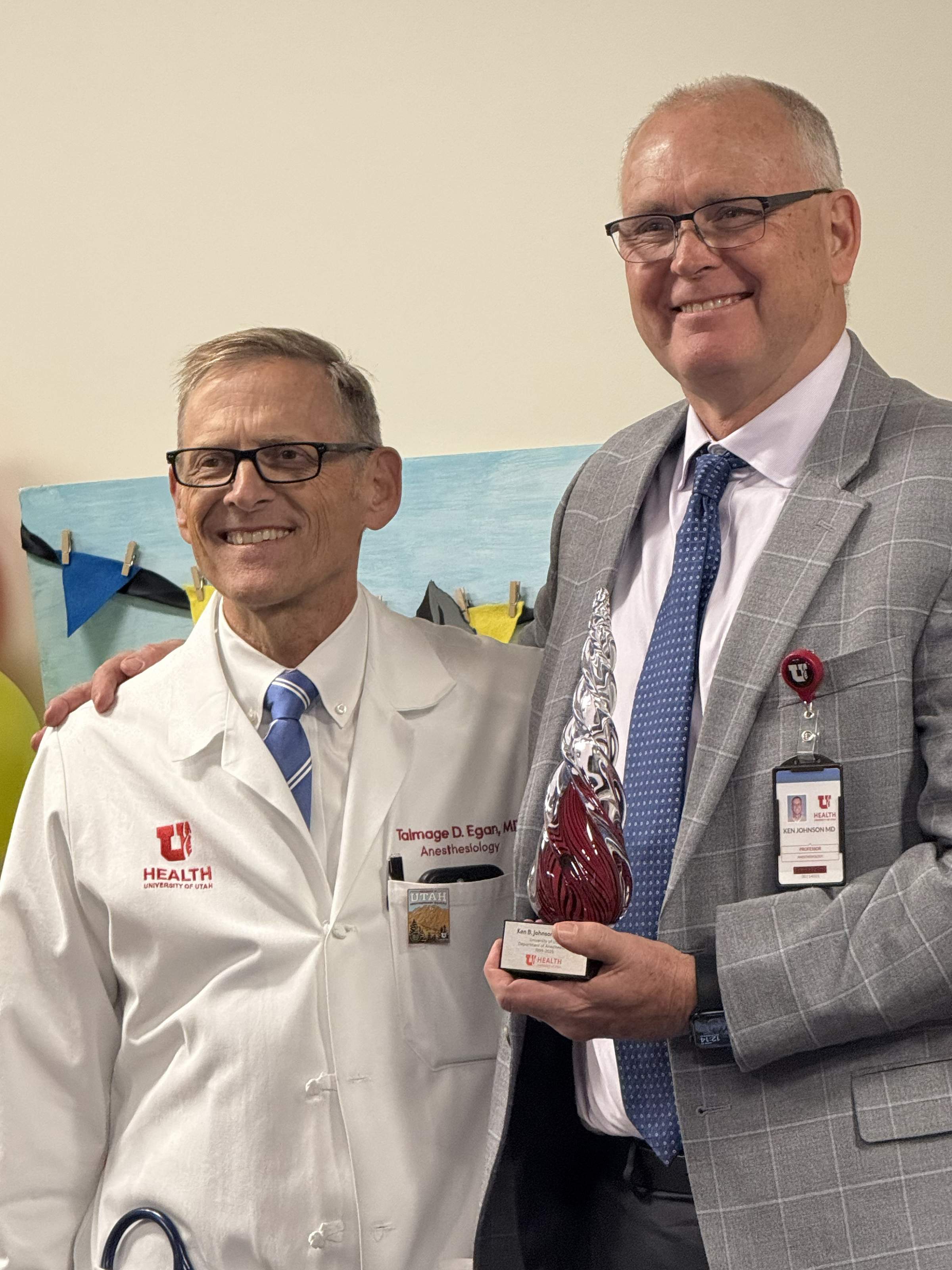 Drs. Talmage Egan (left) and Ken Johnson (right) pose together. Dr. Johnson holds a glass trophy in his hand.