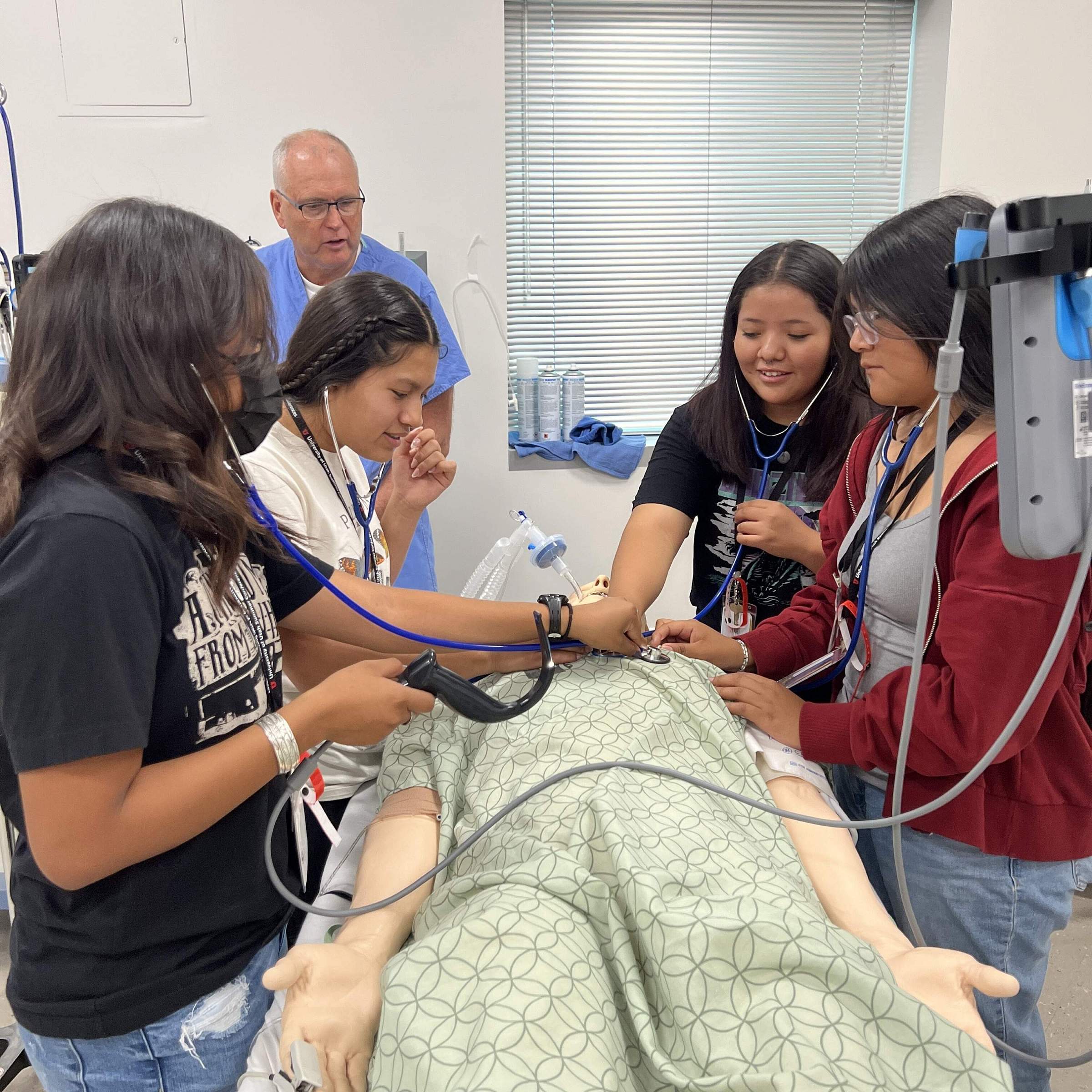 Four elementary school students practicing hearing a heart beat on a mannequin under the guidance of a faculty member.