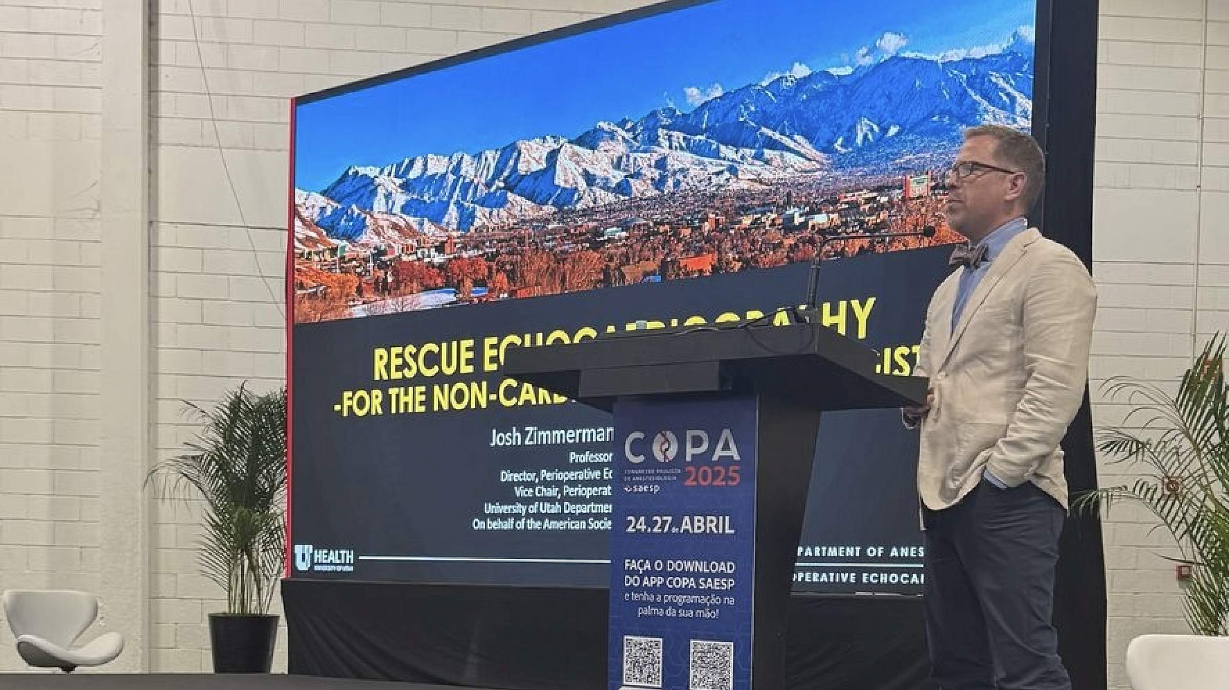Dr. Zimmerman stands to the side of a podium in front of a large presentation screen.